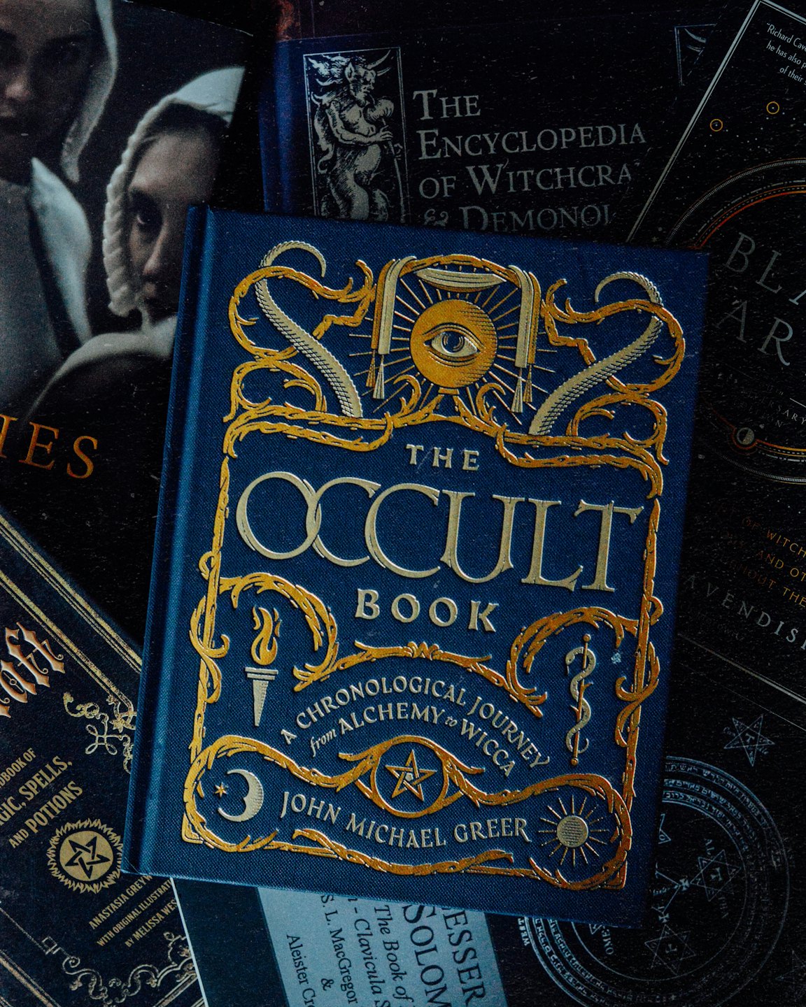 A collection of occult books stacked on a dark surface.